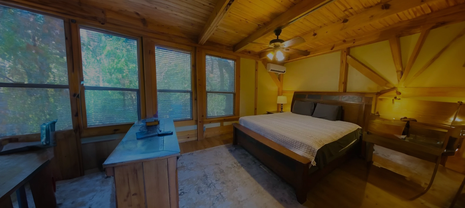 A bedroom with a bed, desk and windows.