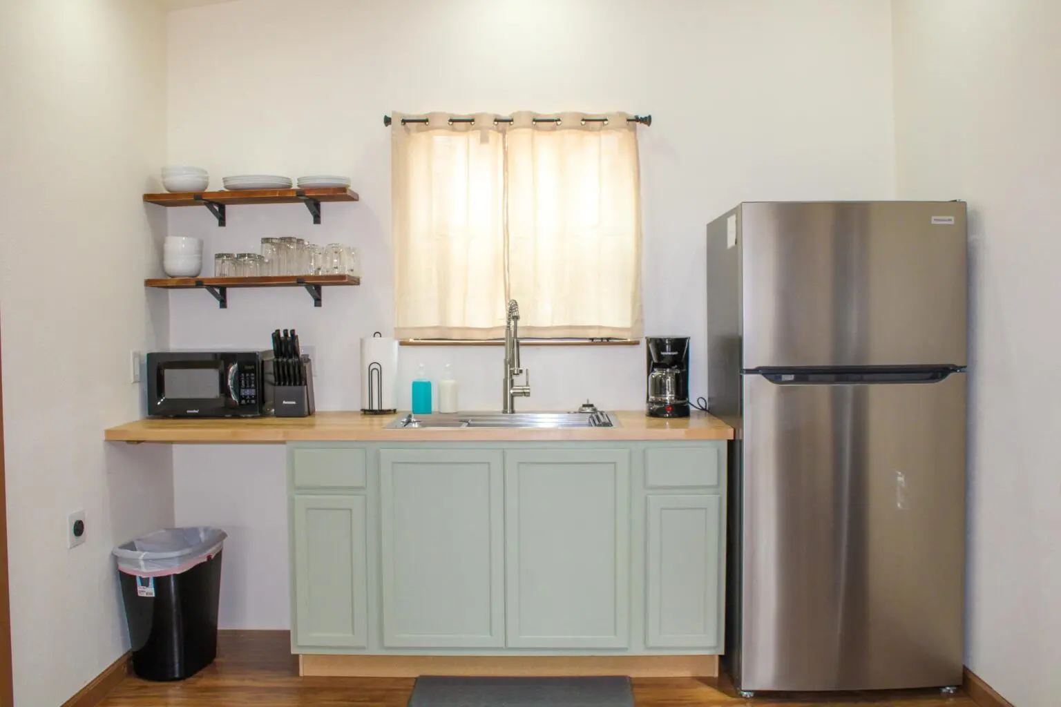 A kitchen with a sink, refrigerator and window.