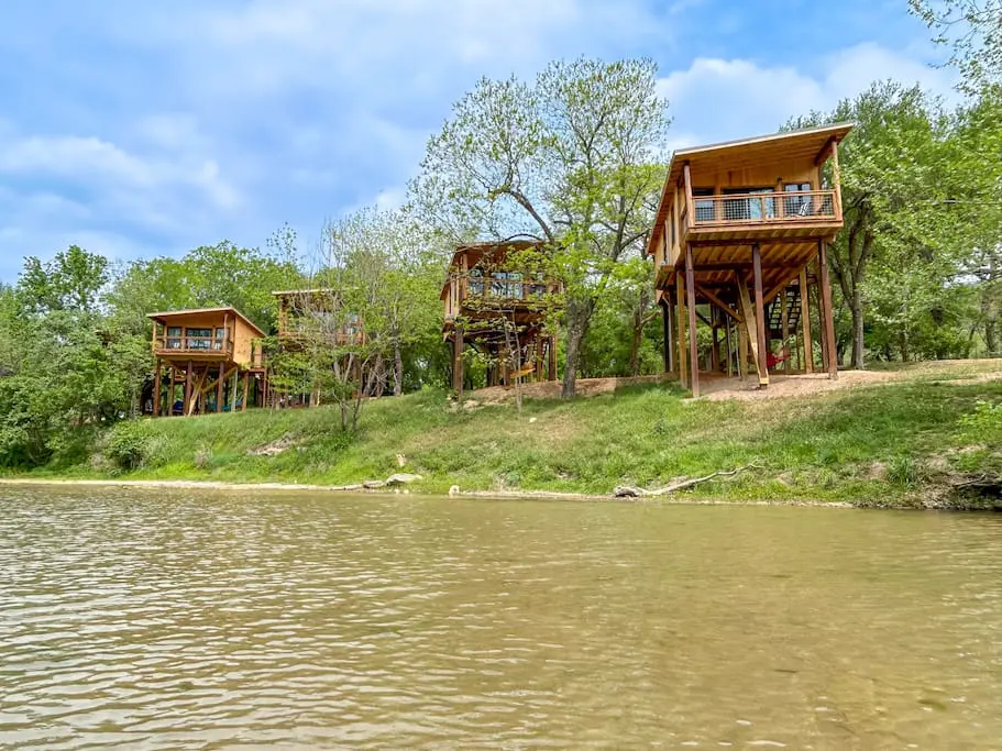 A group of three wooden houses on the side of a river.