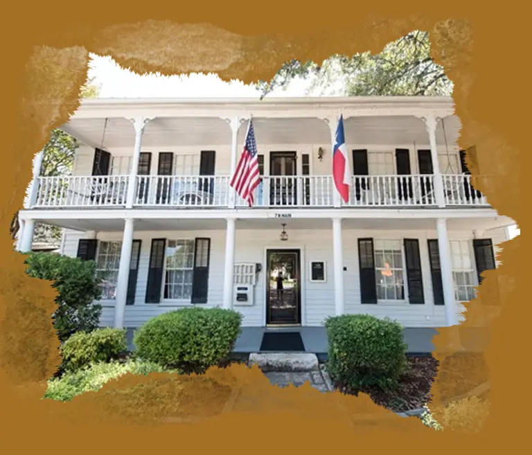 A white two story house with flags on the front porch.